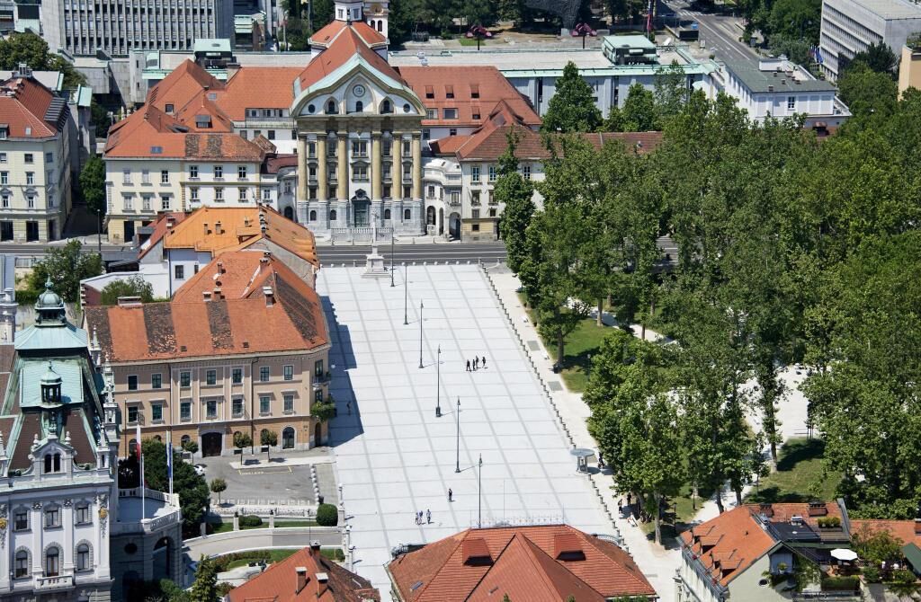 An aerial view of a city square with historic buildings, a large open plaza, and surrounding trees.
