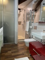 Un baño moderno con cabina de ducha de vidrio, inodoro blanco, tocador rojo y espejo sobre el lavabo.