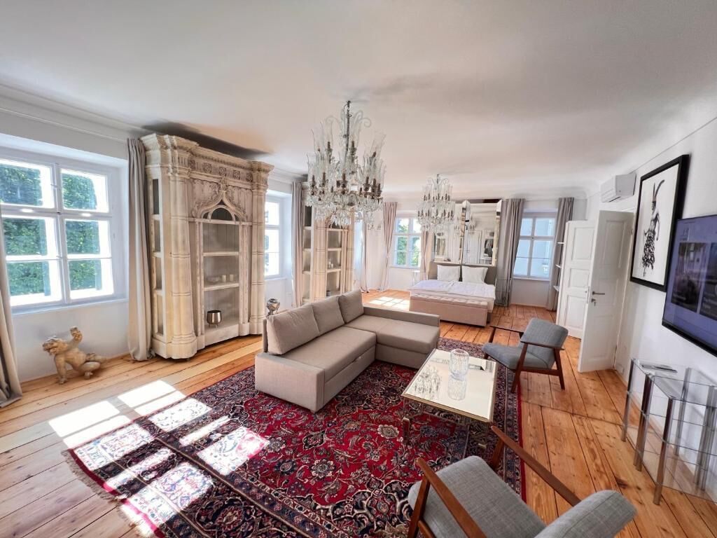 A spacious living room with a large sectional sofa, a red patterned rug, and a chandelier.