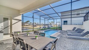 A covered outdoor area with a pool, lounge chairs, and a table with chairs.