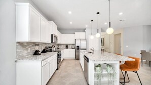 A modern kitchen with white cabinetry, a granite countertop, and pendant lighting. - The Ultimate New 8  Bedroom 6  Bathroom Resort Home (Davenport)