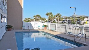 A swimming pool with a white fence, lounge chairs, and a palm tree in the foreground.