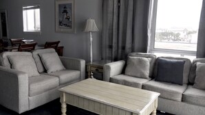 A living room with two grey sofas, a white coffee table, a lamp, and a painting of a lighthouse.
