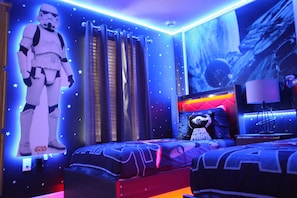 Quarto decorado com tema de Star Wars, com um pôster grande, roupa de cama temática e um recorte de personagem de Star Wars.
