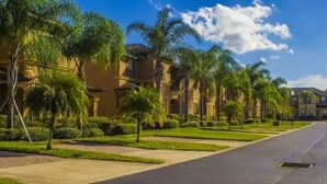 Rua residencial com casas uniformes, palmeiras e gramados bem cuidados.