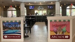 Um saguão de hotel com área de piscina, banheiro e fliperama.