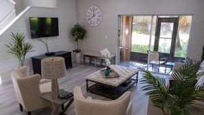 Uma sala de estar moderna com sofá, poltronas, mesa de centro, televisão e uma janela ampla.