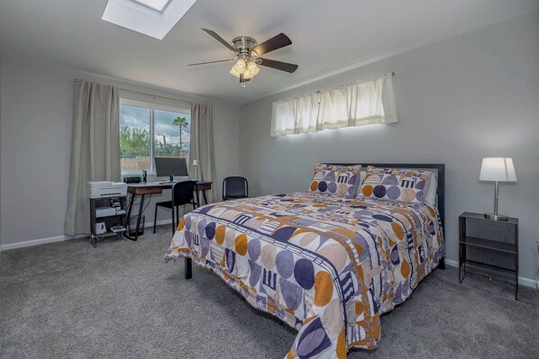 A bedroom with a bed, desk, computer, and a ceiling fan.