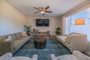 A living room with a sofa, armchairs, a coffee table, a TV, and a ceiling fan.