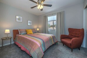 A bedroom with a bed, a chair, a ceiling fan, a window with curtains, and two wall-mounted lamps. - Catalina Velo -Modern home  Catalina Mtn Views (Tucson)