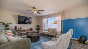 Una sala de estar con un sofá, un sillón, una mesa de centro y un televisor montado en la pared.