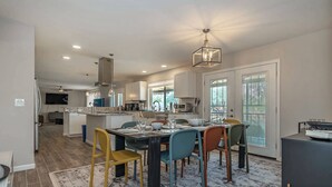 Una cocina moderna con comedor, que incluye una isla central, iluminación colgante y vistas al exterior.