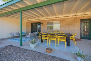 A covered patio with a brick wall, yellow chairs, a table, and a cactus plant. - Catalina Velo -Modern home  Catalina Mtn Views (Tucson)