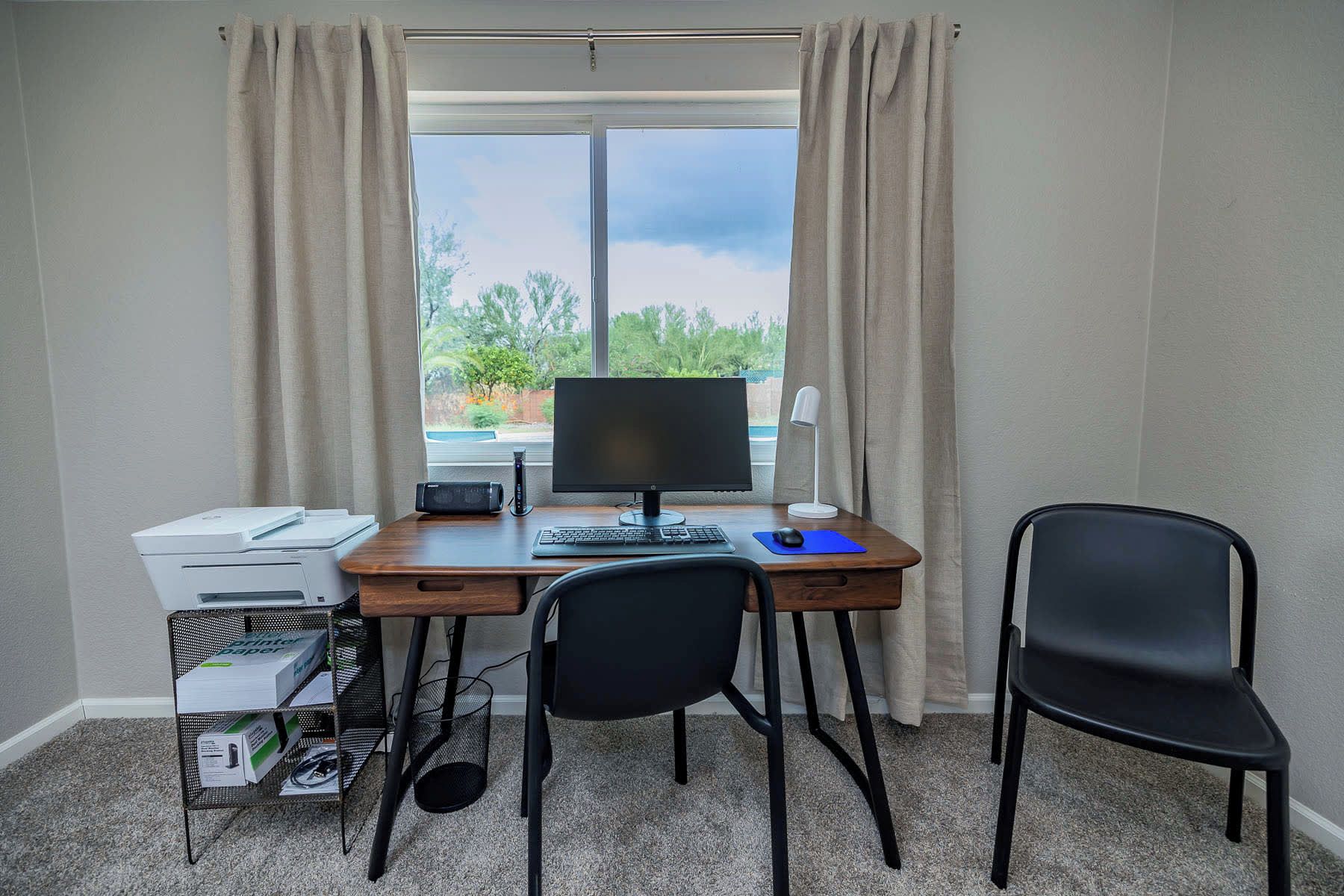 Un petit bureau comprenant un bureau, un ordinateur, une imprimante et deux chaises.