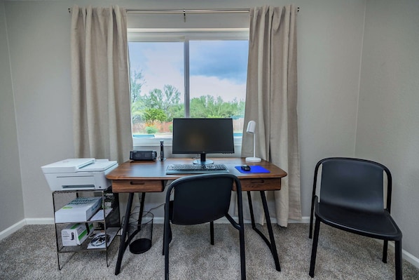 A small office space with a desk, computer, printer, and two chairs.