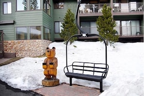 Un banc et une statue d’ours dans un espace extérieur enneigé, avec un bâtiment en arrière-plan.