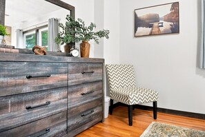 Una habitación con un aparador de madera, una silla, un cuadro y una ventana.