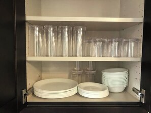 Un meuble de rangement doté d’étagères contenant des bocaux en verre transparent et des assiettes blanches.