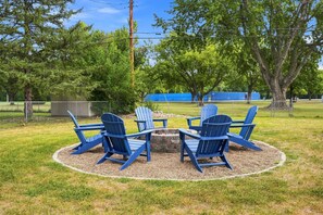 A circular seating area with four Adirondack chairs around a central fire pit, surrounded by a gravel border.