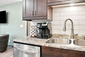 Una cocina moderna con lavavajillas integrado, cafetera y pileta de acero inoxidable.