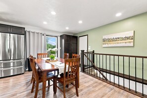 Un comedor con mesa y sillas de madera, una cocina con electrodomésticos de acero inoxidable y vistas a través de un ventanal.
