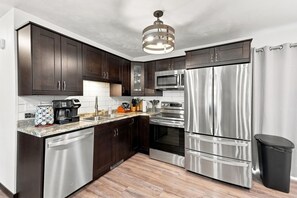 A modern kitchen with dark wood cabinets, stainless steel appliances, a dishwasher, and a trash can.