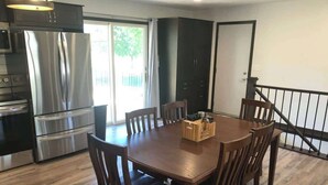 A modern kitchen with stainless steel appliances, a dining table with six chairs, and a view of the outdoors through a sliding door.