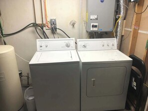 Deux machines à laver à chargement frontal sont installées dans une buanderie, avec la tuyauterie et les branchements électriques apparents.