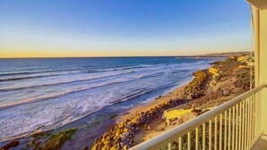 Blick aufs Meer vom Balkon mit Strand und felsiger Küste, bewölkter Himmel.