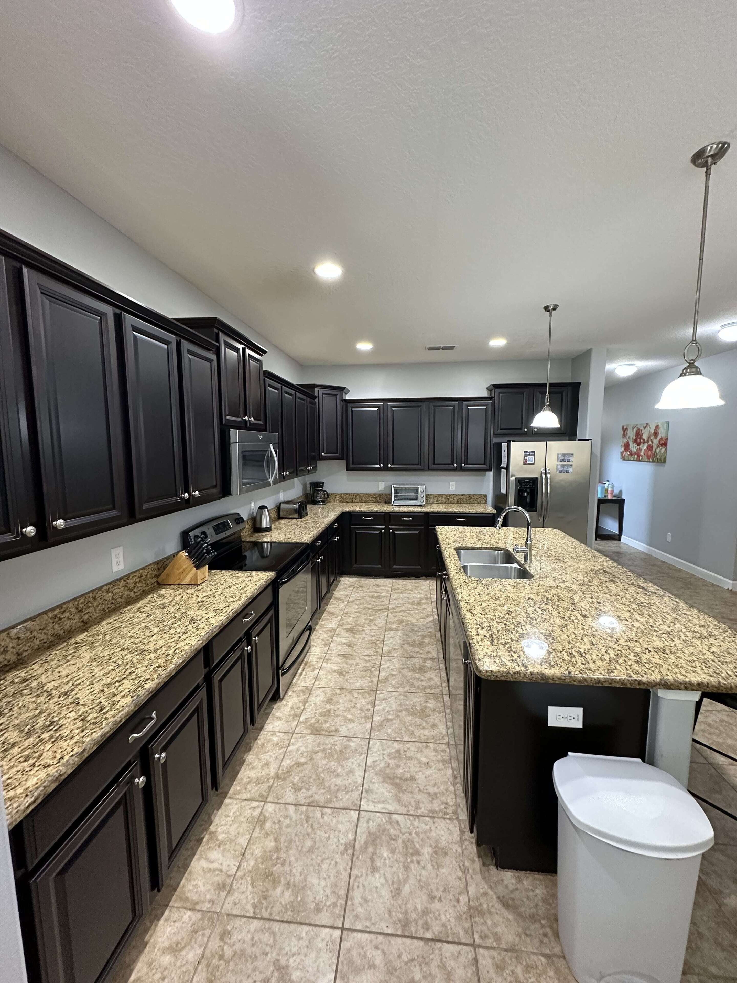 A modern kitchen with dark cabinetry, granite countertops, stainless steel appliances, and pendant lighting.