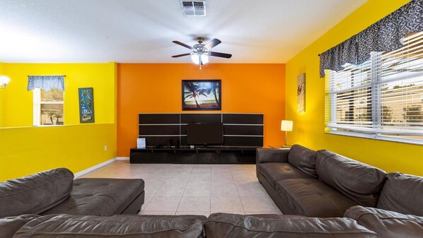 Relax in this stylish living room with a large flat-screen TV, two comfortable sofas, and a ceiling fan for ventilation.