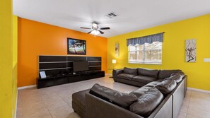 Relax in this stylish living room with a large flat-screen TV, comfortable sofa, and ceiling fan.
