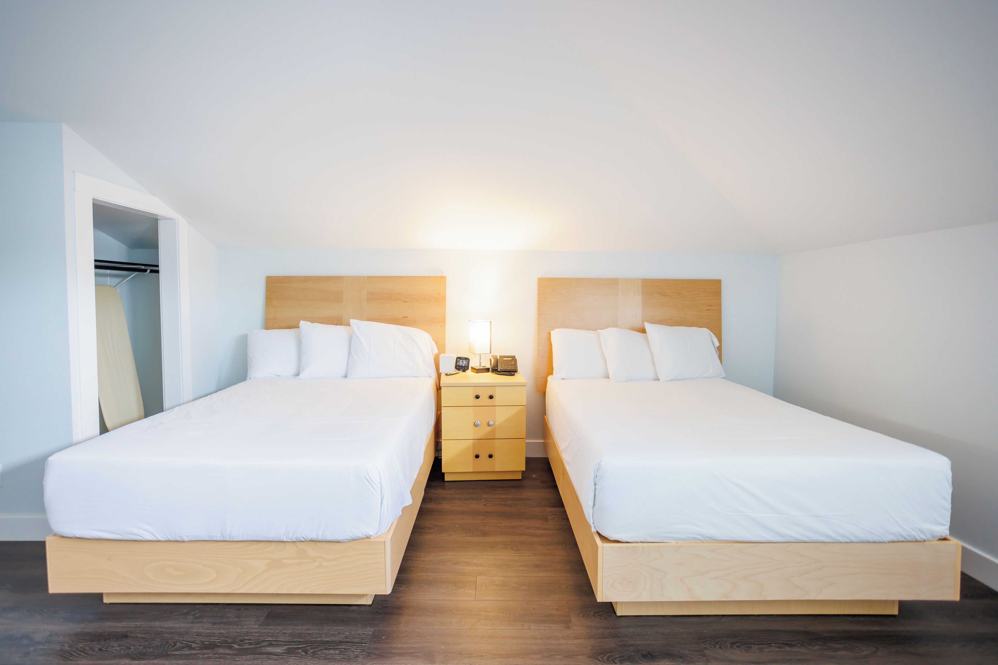 Een tweepersoonskamer met twee bedden, een houten nachtkastje en een kledingkast.