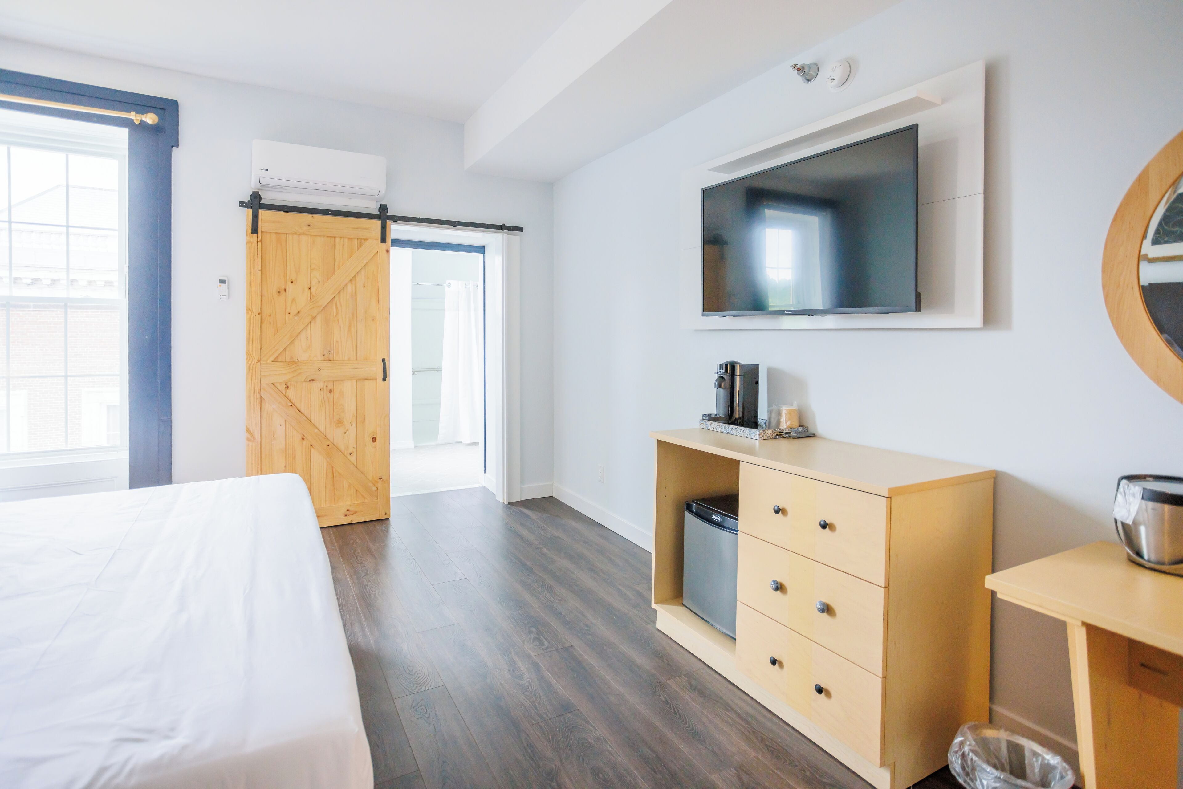 A modern bedroom with a bed, a wooden wardrobe, a TV mounted on the wall, and a sliding door leading to a balcony.