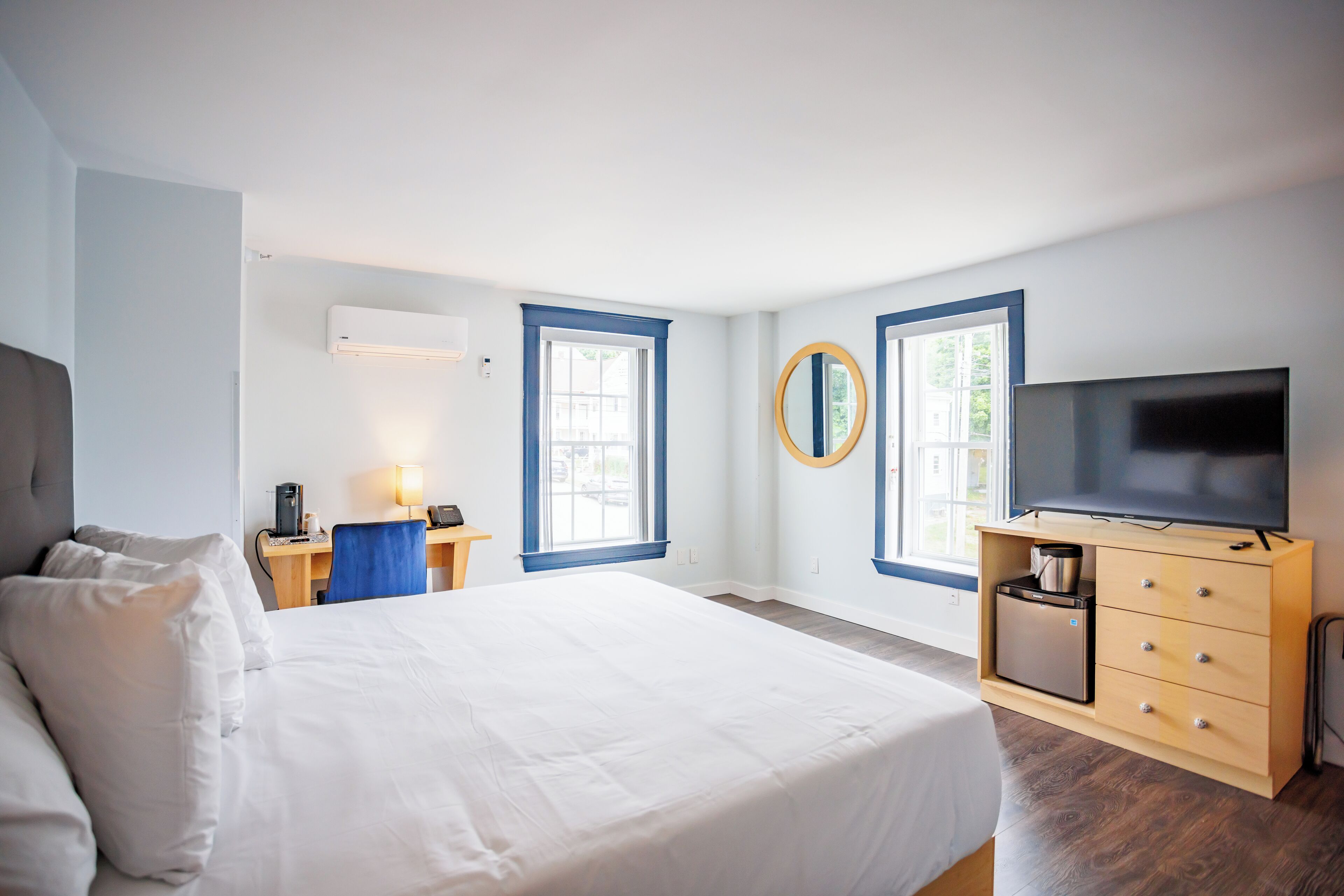 A hotel room with a large bed, a desk with a chair, a television, and a minibar.