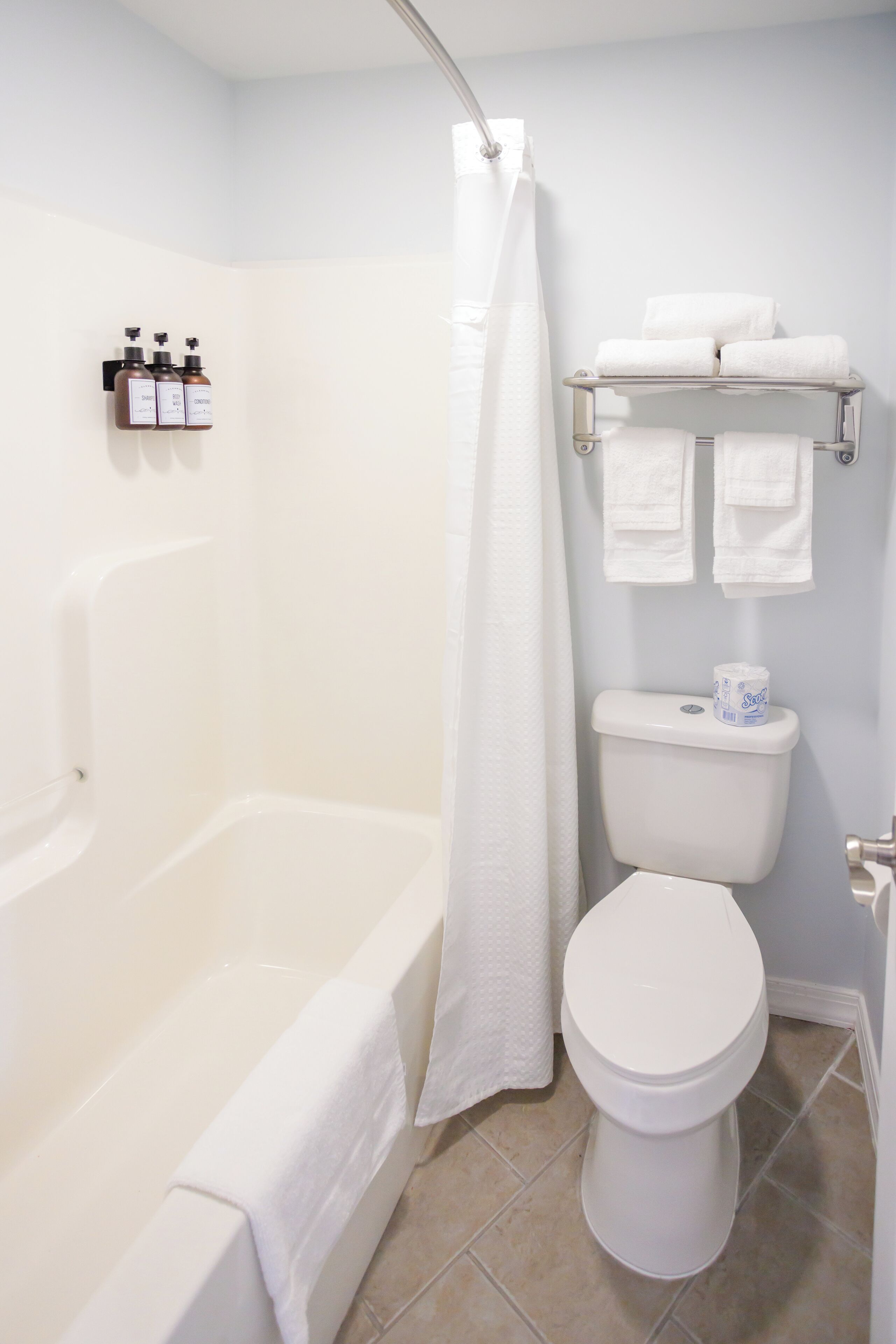 A bathroom with a bathtub, toilet, and a towel rack with towels.