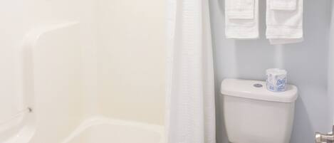 A bathroom with a bathtub, toilet, and a towel rack with towels.