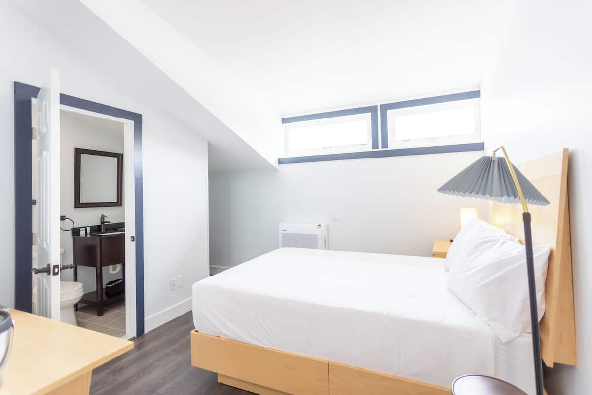 A hotel room with a bed, bedside table, lamp, and a view of the bathroom.