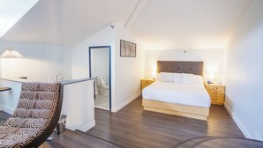 Ein modernes Schlafzimmer mit einem großen Bett, einem gebogenen Sessel, einem Nachttisch und einem Beistelltisch.