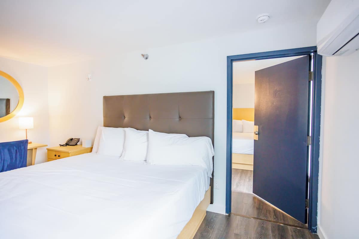 A hotel room with a large bed, bedside tables, a mirror, and an open door leading to another room.