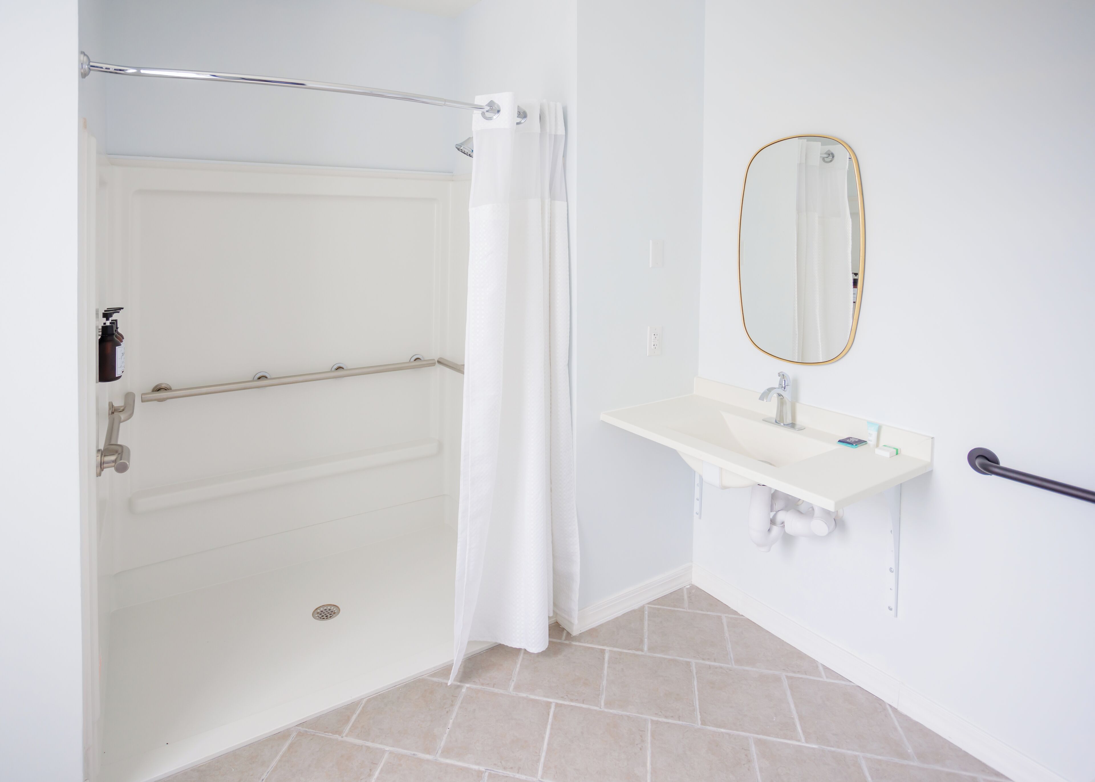 A bathroom with a shower, a white sink, a mirror, and a grab bar.