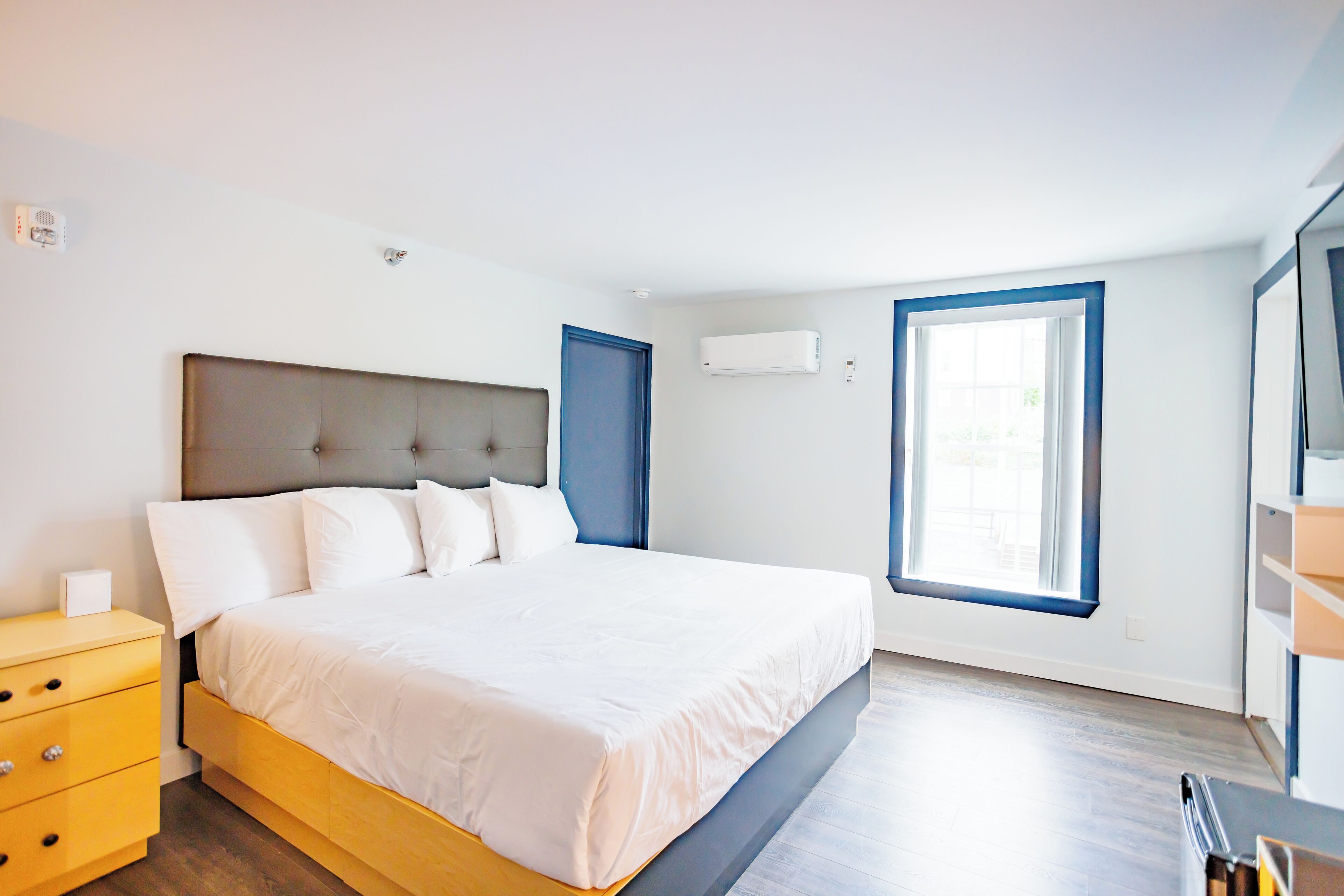 A bedroom with a bed, a nightstand, a window, and an air conditioning unit.