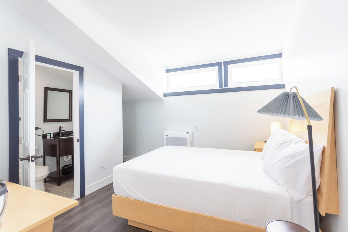Une chambre à coucher avec un lit, une table de chevet, une lampe et une vue sur la salle de bain.
