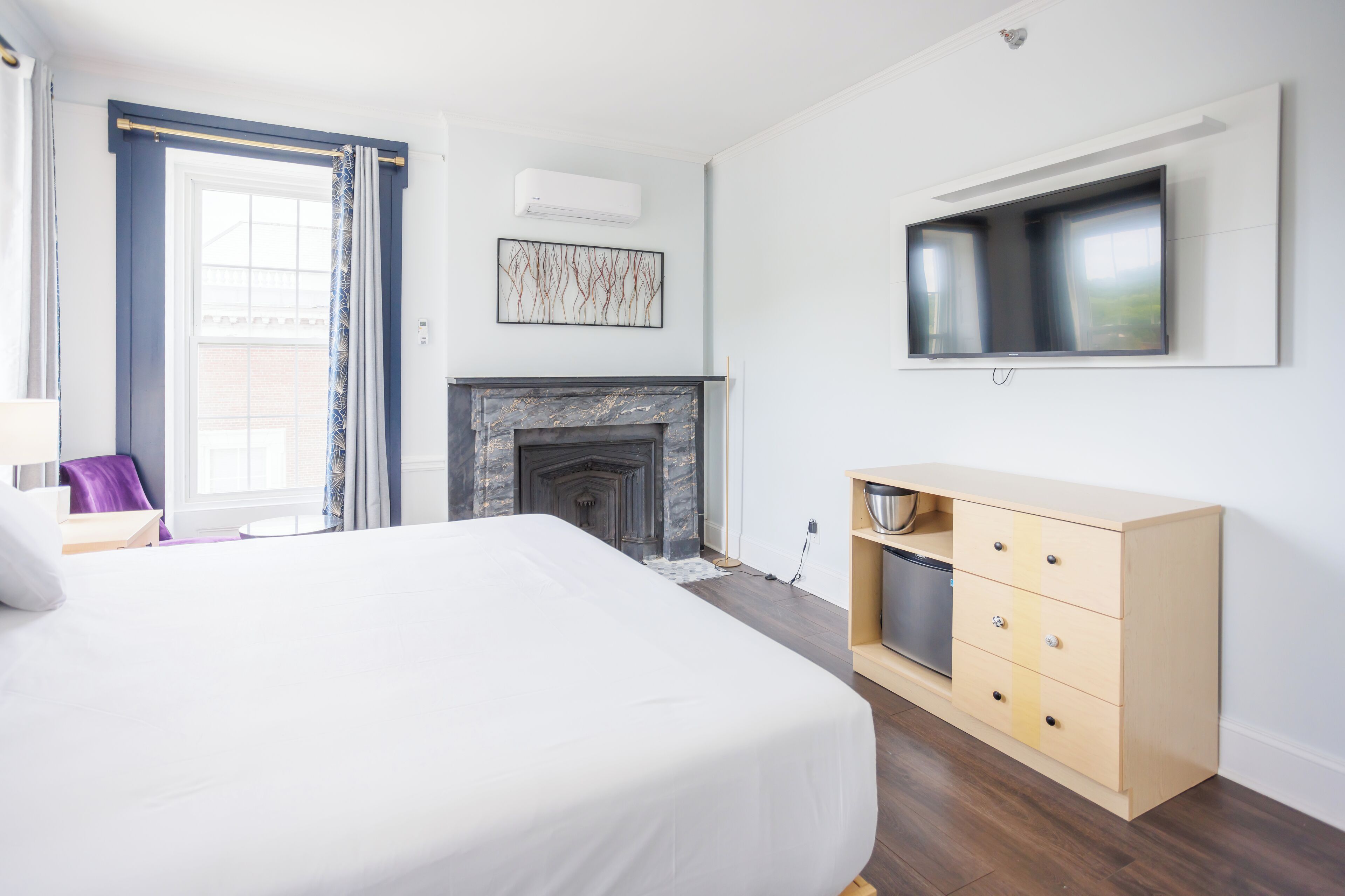 Une chambre d’hôtel moderne dotée d’un grand lit, d’une cheminée, d’un téléviseur fixé au mur et d’une commode en bois.
