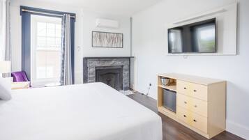 Une chambre d’hôtel moderne dotée d’un grand lit, d’une cheminée, d’un téléviseur fixé au mur et d’une commode en bois.