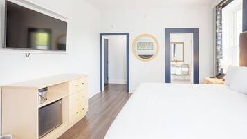 A modern hotel room with a large bed, a TV mounted on the wall, a wooden dresser, and a bathroom visible through an open door.