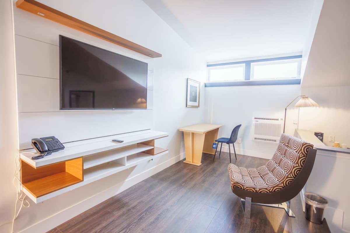 A modern living room with a flat-screen TV mounted on the wall, a wooden desk, a patterned armchair, and a small trash can.