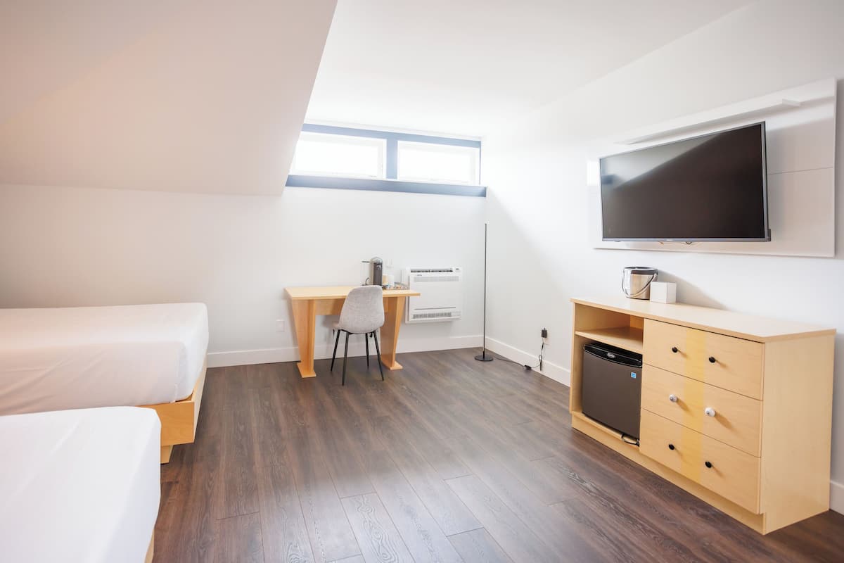 A modern hotel room with a bed, desk, chair, TV, and storage unit.