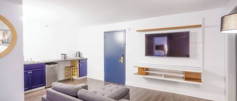 A modern living room with a grey sofa, a flat-screen TV mounted on the wall, and a wooden dining table.