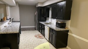 Una cocina compacta con armarios oscuros, encimera de granito, lavavajillas y cubo de basura.